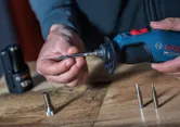 A person attaches a metal tip to a cordless soldering iron on a wooden surface.