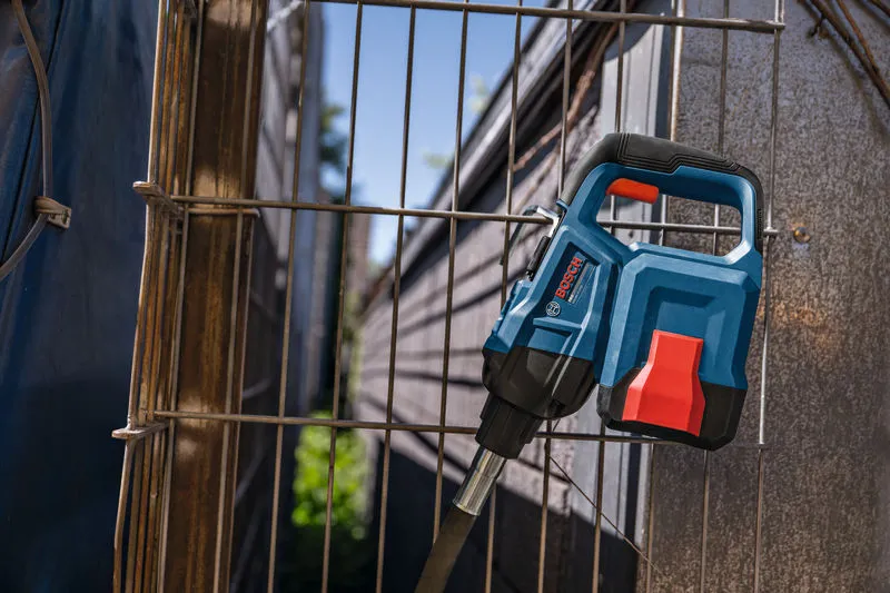 A blue and red power tool rests against a metal wire fence outdoors.