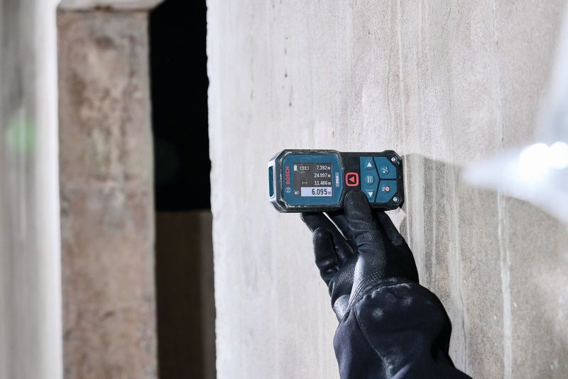Person wearing safety equipment uses a laser measure against a concrete wall.