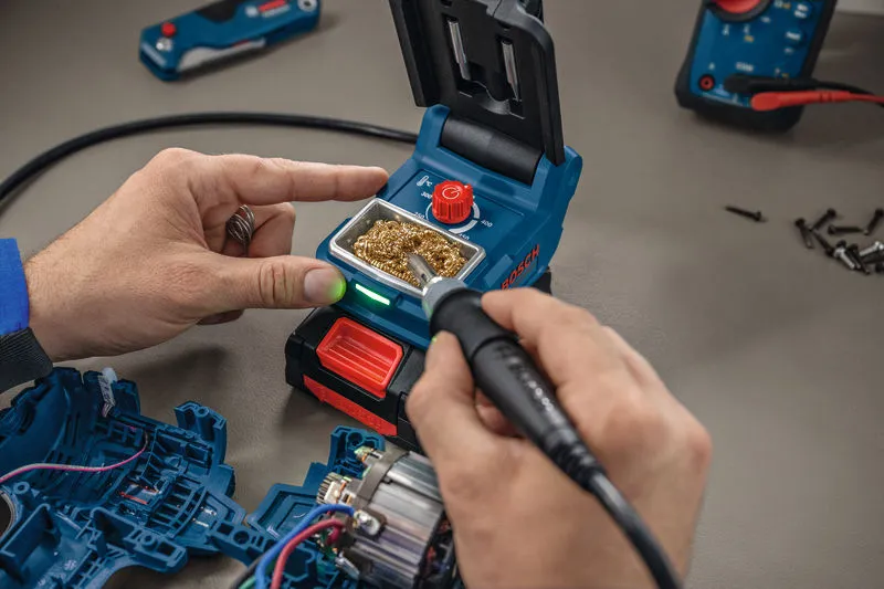 A person uses a cordless soldering iron to work on electronic components.
