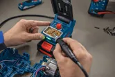 A person uses a cordless soldering iron to work on electronic components.