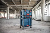 Stacked wheeled contractor cart with cases stands in a large unfinished building.