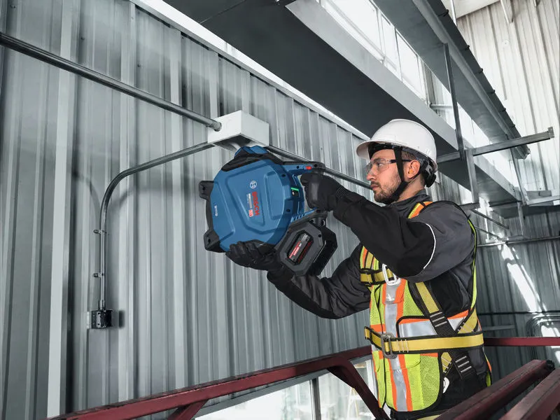 A person wearing safety equipment drills into a metal wall inside an industrial building.