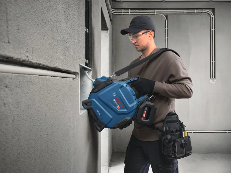 A person wearing safety equipment pulls electrical cable into a wall-mounted box.