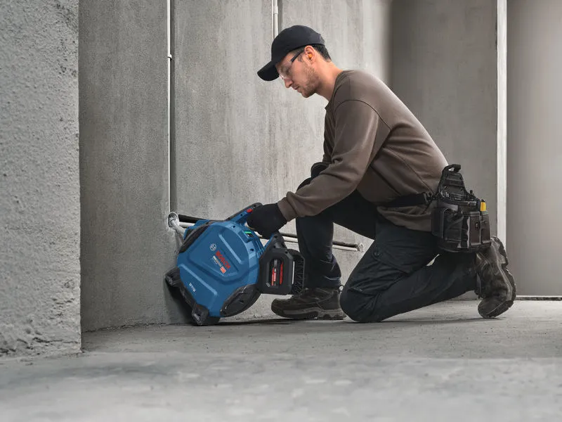 A person wearing safety equipment cuts a groove in concrete with a power tool.