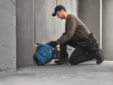 A person wearing safety equipment cuts a groove in concrete with a power tool.