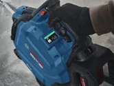 A person wearing safety equipment operates a blue cordless tool with a digital display.