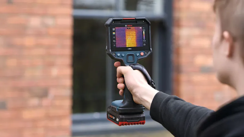 A person uses a thermo camera to scan the exterior of a building.