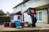 Thermal camera and smartphone with thermal imaging app on a masonry wall outside a house.