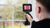 Person holding a thermo camera to scan a window frame indoors.