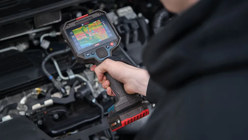 A person uses a thermo camera to inspect an engine compartment.