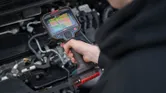 A person uses a thermo camera to inspect an engine compartment.