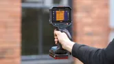 Person holds a thermo camera in front of a building window.