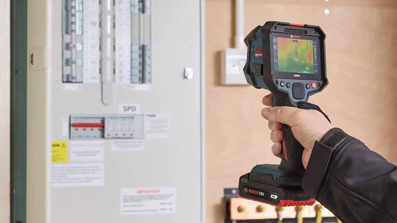 Person wearing safety equipment scans an electrical panel with a thermo camera.