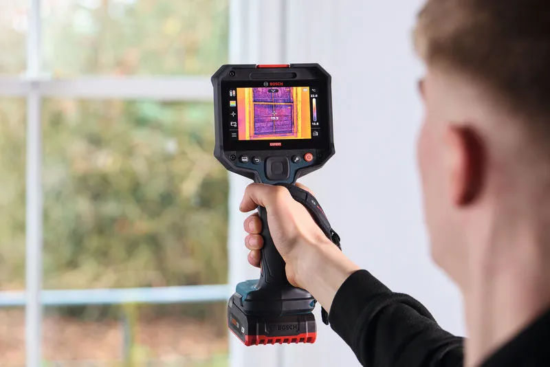 Person operating a thermo camera device to scan insulation near a window.
