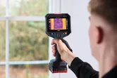 Person operating a thermo camera device to scan insulation near a window.