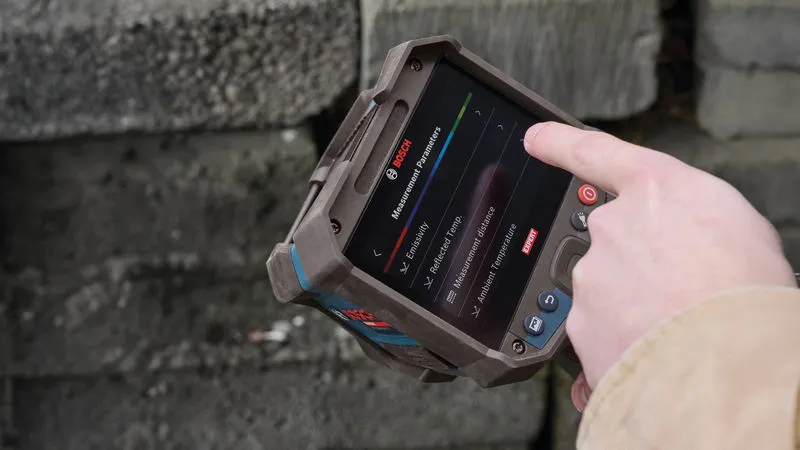 Person holds a thermo camera near a stone wall and selects options on the touchscreen.