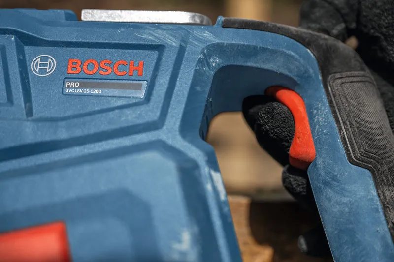 Person wearing safety equipment grips a blue power tool handle with a red trigger.