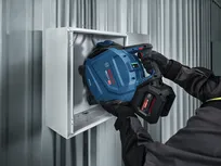 A person wearing safety equipment uses a cordless power tool to work inside a metal box.