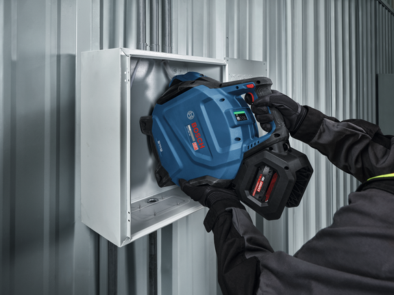 A person wearing safety equipment uses a cordless power tool to work inside a metal box.
