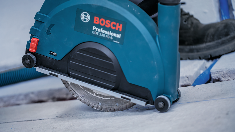 A person wearing safety equipment uses a circular saw to cut concrete.