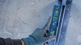 Person wearing safety equipment checks level alignment on a metal rail.