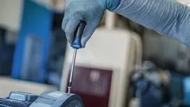 Person wearing safety equipment tightens a screw with a screwdriver on machinery.
