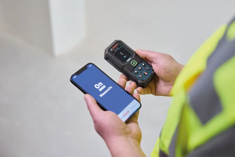 Person wearing safety equipment uses a laser measure while operating a mobile app.