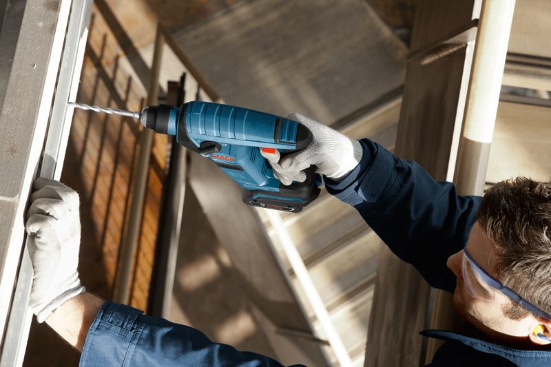 Person wearing safety equipment drills into metal framing with a cordless power tool.