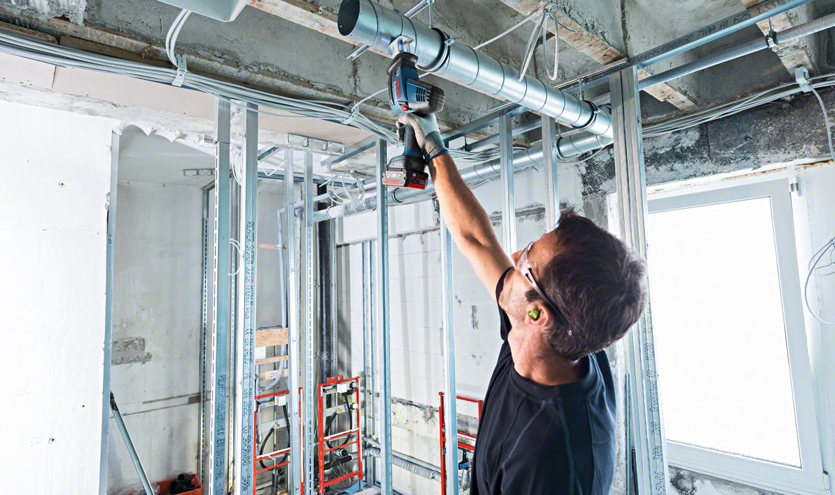 A worker uses a Bosch Professional drill to install ducting in a construction site.