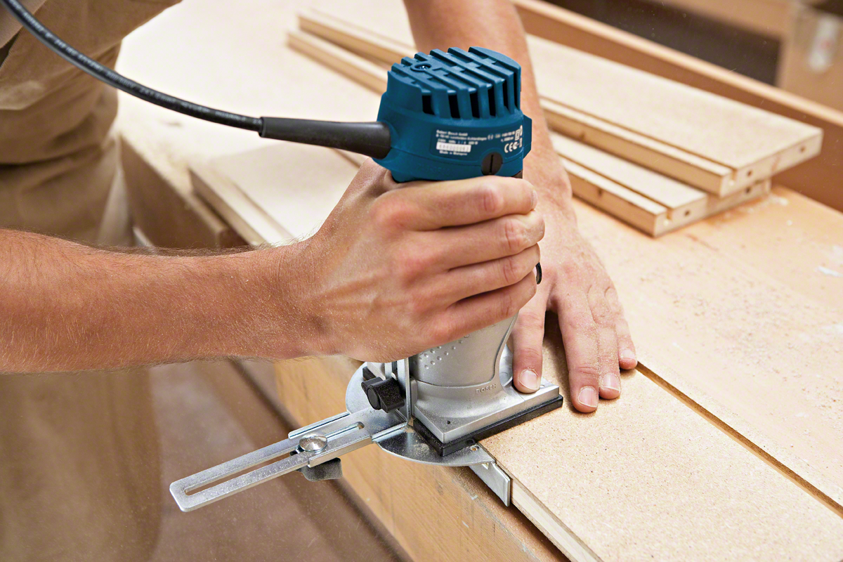 A Bosch Professional router is used on a wooden board with guiding pieces nearby.