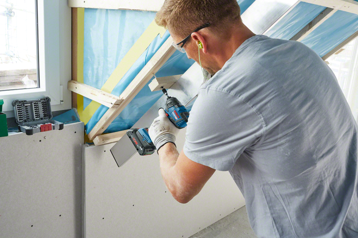 A person uses a Bosch Professional drill on a construction site with drywall.