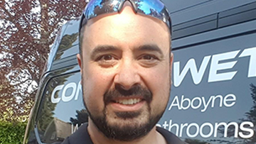 A man with sunglasses smiles in front of a van with bathroom service branding.