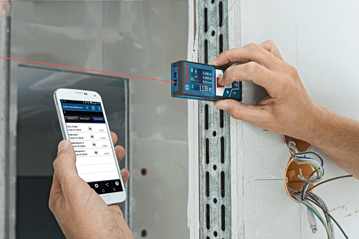 A person measures a wall with a Bosch laser distance meter and checks data on a smartphone.
