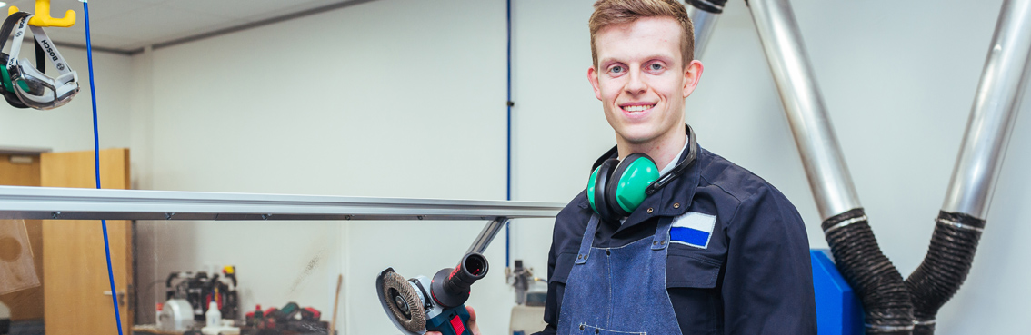 A smiling man in work attire holds a Bosch tool in a workshop setting.