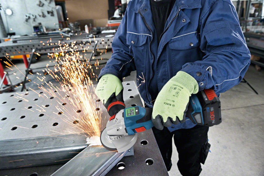 A worker in a blue jacket uses a Bosch Professional grinder, creating sparks on metal.