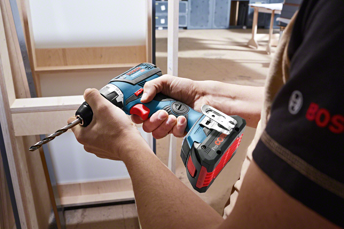 A Bosch Professional cordless drill is held, ready to use, in a workshop setting.