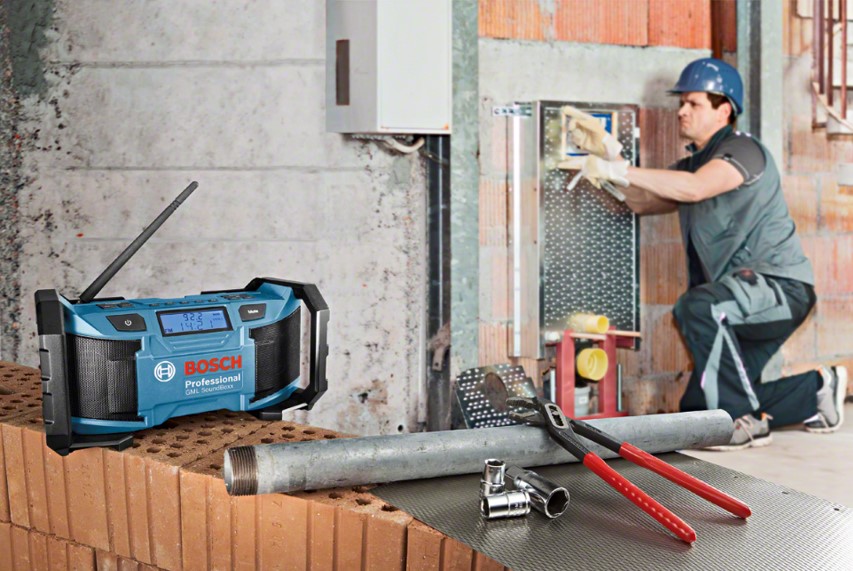 A blue Bosch Professional radio sits on bricks; a worker kneels nearby, using tools.