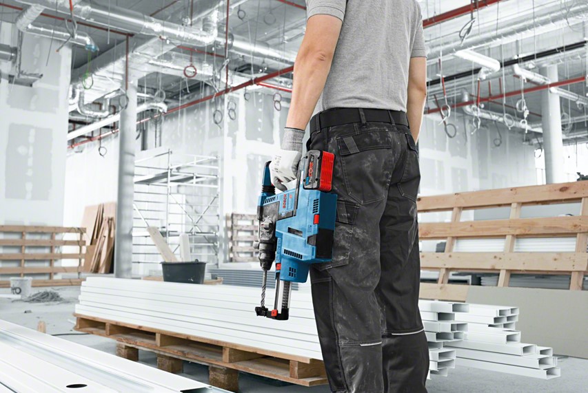 A man in gray shirt holds a blue Bosch Professional tool in a construction site.