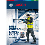 A worker in a yellow vest drills into a wall in a construction site, with tools nearby.