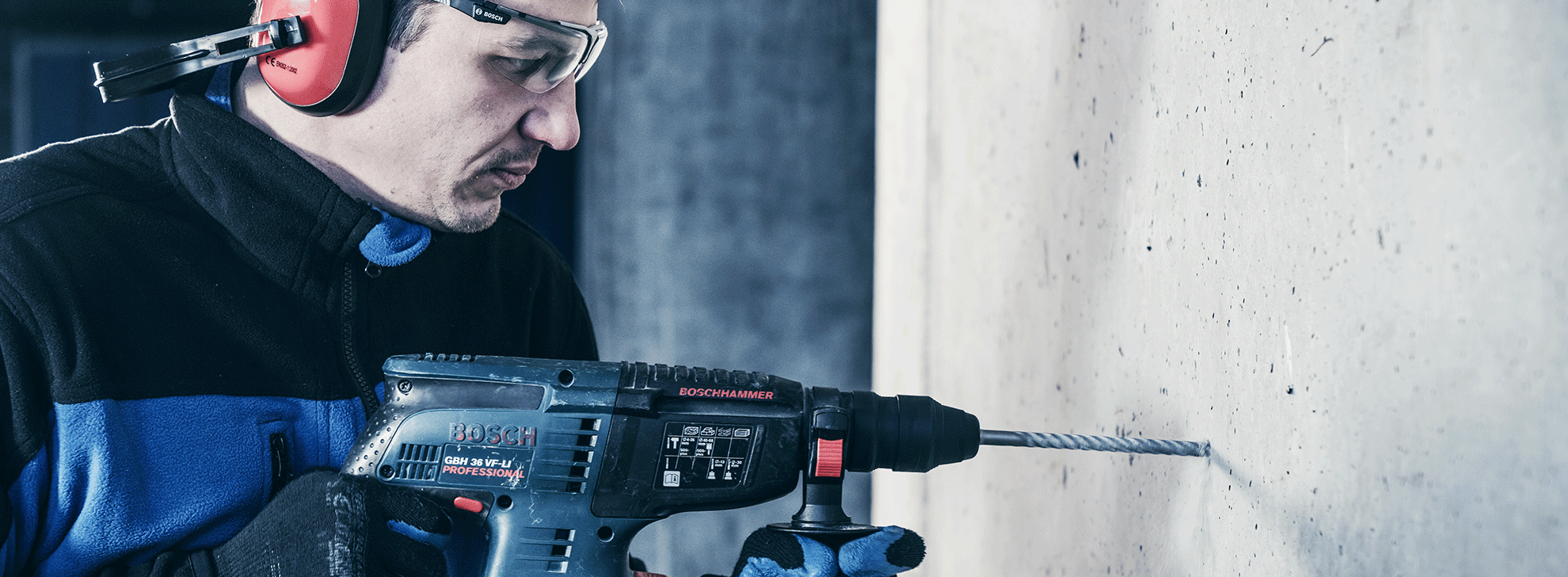 A man with safety glasses is drilling with a blue Bosch Professional drill.