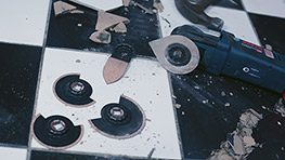 A Bosch Professional tool lies on a black and white floor, surrounded by broken tiles.