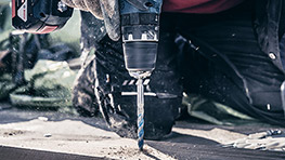 A Bosch Professional drill is being used on a wooden surface, with dust flying around.