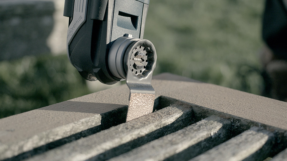 A Bosch Professional tool is cutting a wooden plank outdoors in bright sunlight.