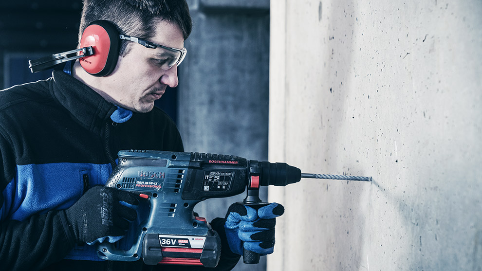 A man in safety gear uses a Bosch Professional hammer drill on a concrete wall.