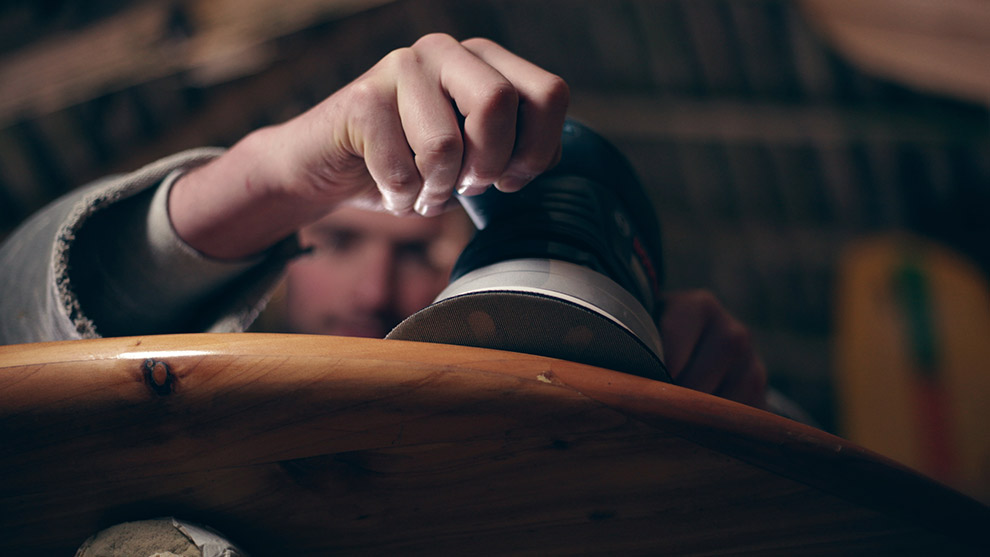A person using a Bosch professional sander on a wooden surface in a workshop.
