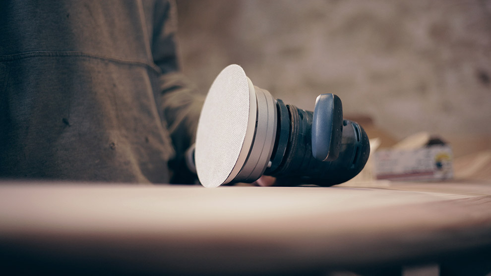 A Bosch Professional sander rests on a wooden surface, with a hand nearby.