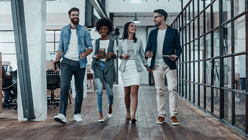 Four professionals walk together in an office, smiling and holding tablets and folders.