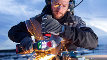 A man uses a Bosch Professional tool, creating sparks at dusk with protective gear.