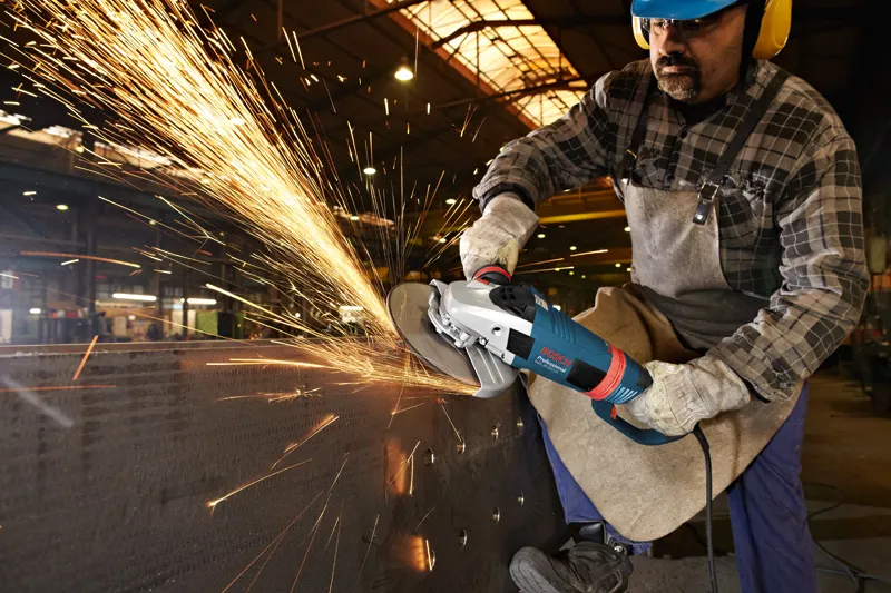 A person wearing safety equipment grinds metal, creating a shower of bright sparks.